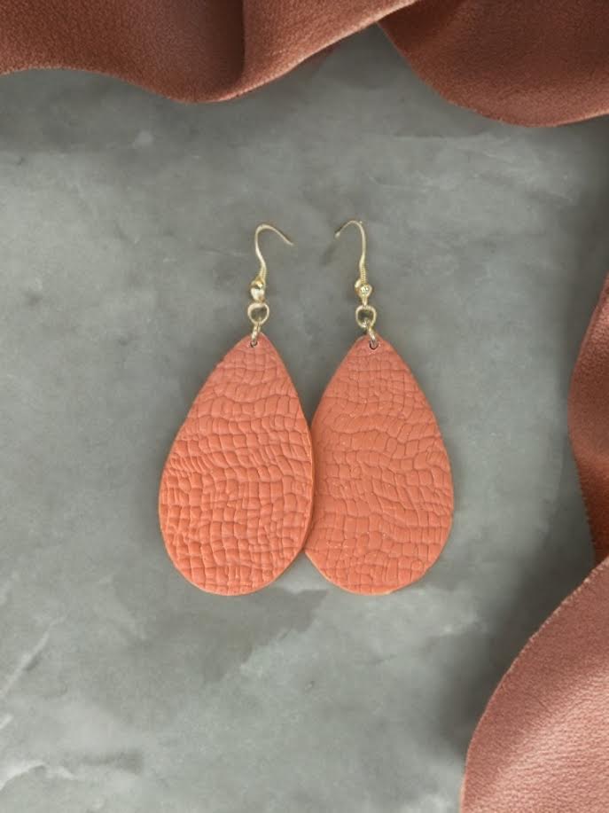 Terra Cotta-colored teardrop earrings on a gray surface with brown fabric around.