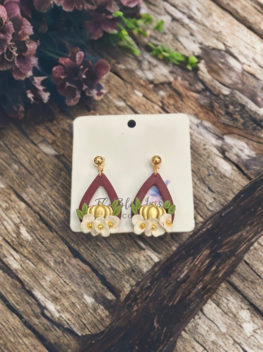 Polymer clay teardrop earrings with gold pumpkin, white flowers, and green leaves on burgundy base