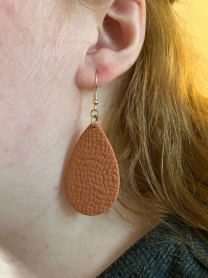 Terra Cotta leather looking teardrop polymer clay earrings being worn by a girl with red hair. 