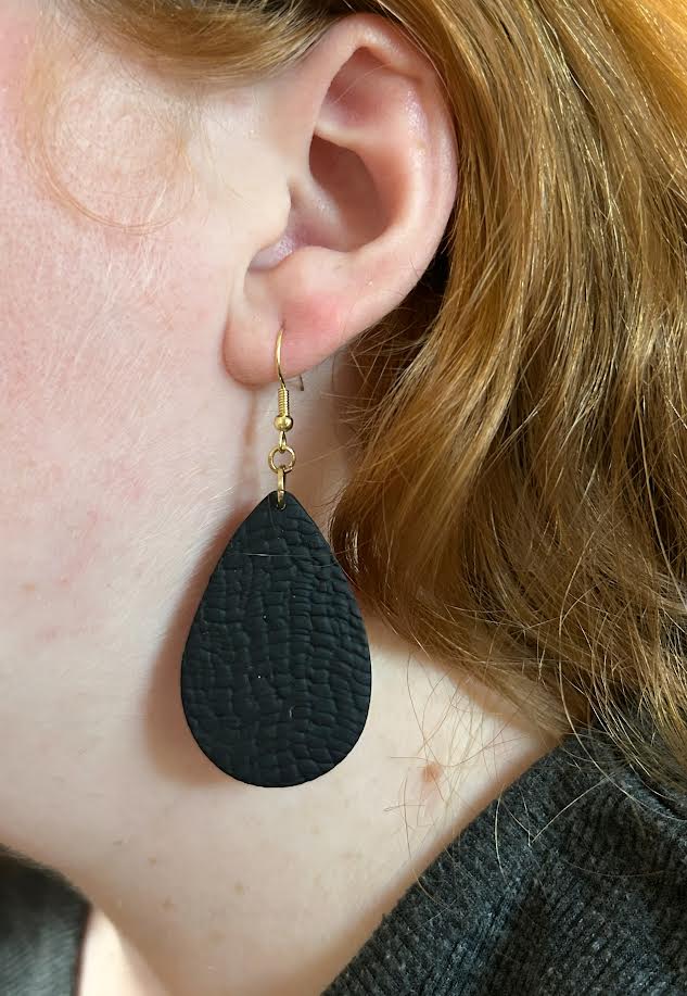 Black teardrop earrings worn by a person with red hair.